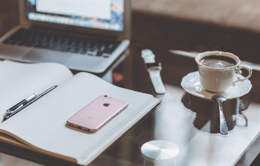 an open notebook on a desk in front of a laptop with a cup of coffee to the right