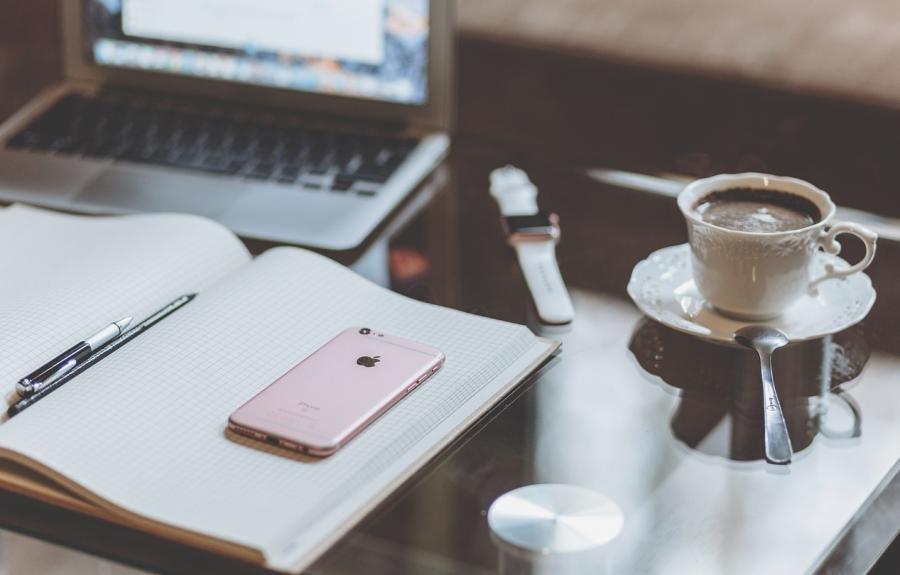 an open notebook on a desk in front of a laptop with a cup of coffee to the right